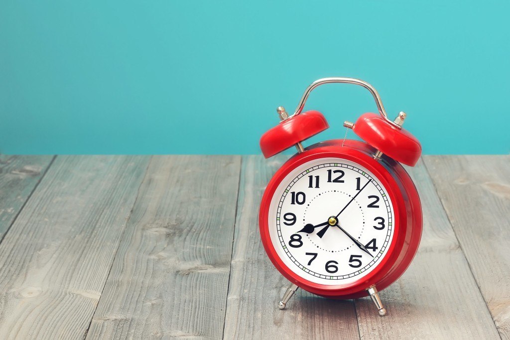 Red retro alarm clock on a wooden table on a blue background. The sound of the alarm.