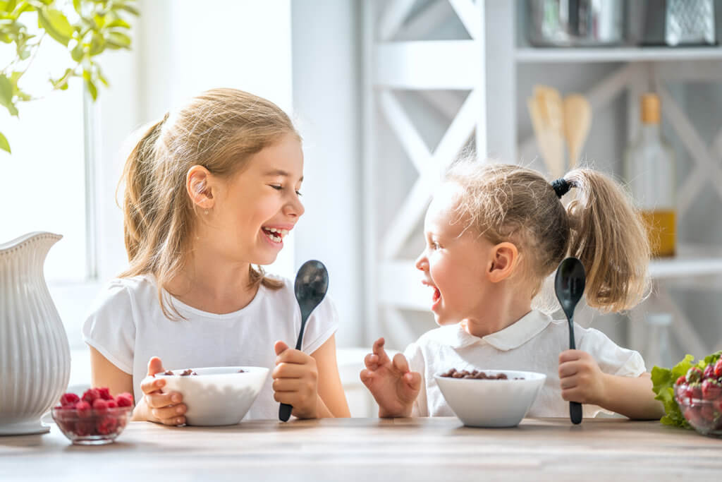 Two young girls sitting at the table eating breakfast